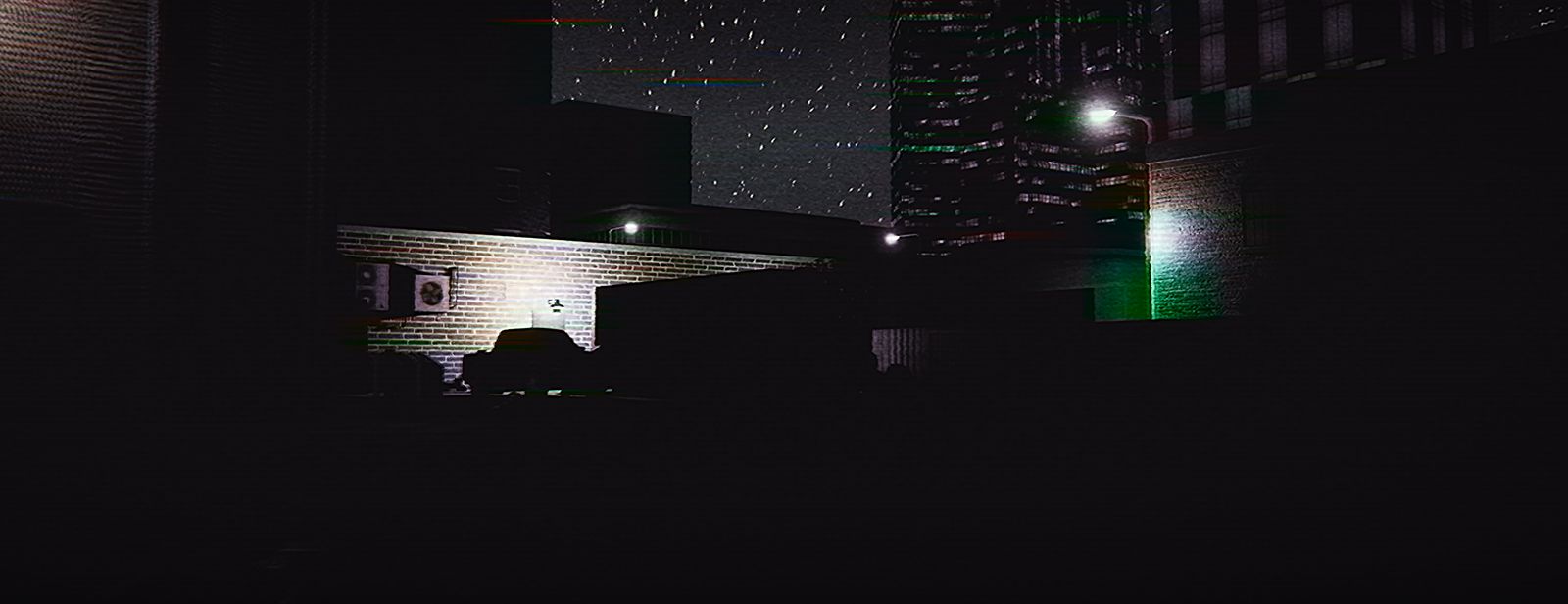 The back of the building at night with the city rising behind it