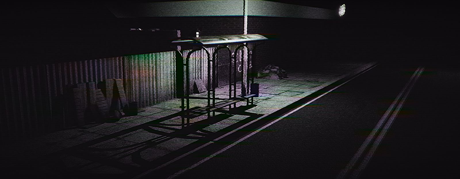 A bus shelter lit from above on an empty street, graffiti on the hoarding behind